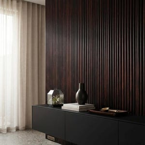 May include: A dark brown wooden slatted wall panel behind a matte black floating cabinet. On the cabinet sits a glass geometric terrarium with a small plant, a stack of two white books, a black vase, and a wooden tray with a gold spoon.