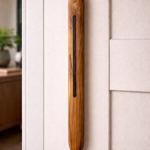 May include: A vertical wooden door pull with a natural finish and a dark, contrasting inlay. The elongated, rounded design is mounted on a white door, showcasing the wood's grain and texture. This decorative hardware adds a touch of natural elegance.