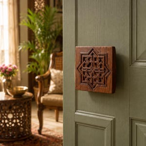 Puede incluir: Un aldaba rectangular de madera marrón oscuro con un intrincado diseño geométrico está montada en una puerta verde. La detallada talla de la aldaba contrasta con la superficie lisa de la puerta, sugiriendo una mezcla de estilos.