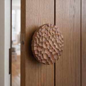 May include: A close-up of a wooden door with a large, round, carved wooden door knob. The knob has a textured, geometric pattern. The door and knob are a warm brown color.