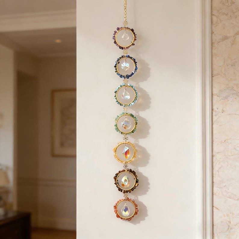 May include: A decorative hanging crystal suncatcher with seven circular elements. Each circle features a different color of gemstones and a dangling crystal. The circles are connected by a gold chain, creating a vertical display.
