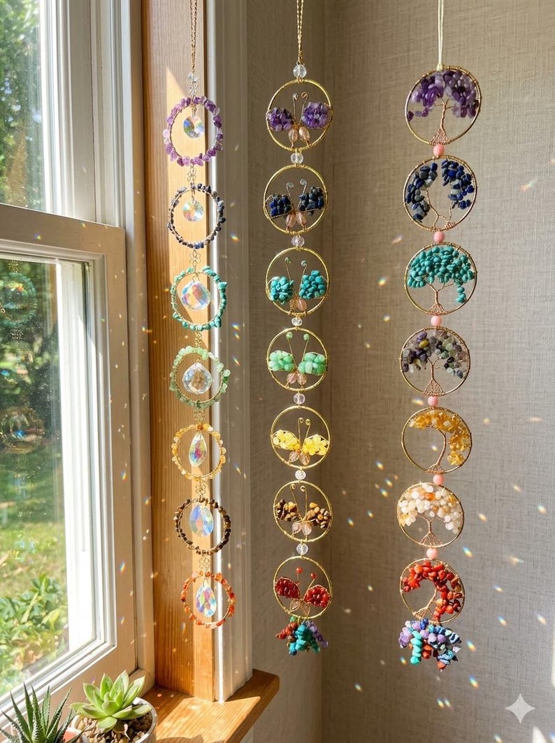 May include: A collection of hanging crystal suncatchers and gemstone ornaments. The suncatchers feature colorful crystals and beads, while the ornaments showcase butterfly and tree designs made of various gemstones. The pieces are suspended by gold-colored chains.