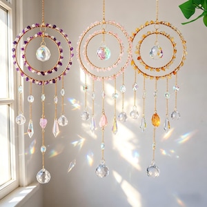 May include: Three hanging suncatchers with gold-colored rings, adorned with crystals and beads in purple, pink, and yellow hues. Each suncatcher features a central crystal ball and dangling crystal pendants, creating a decorative and shimmering effect.