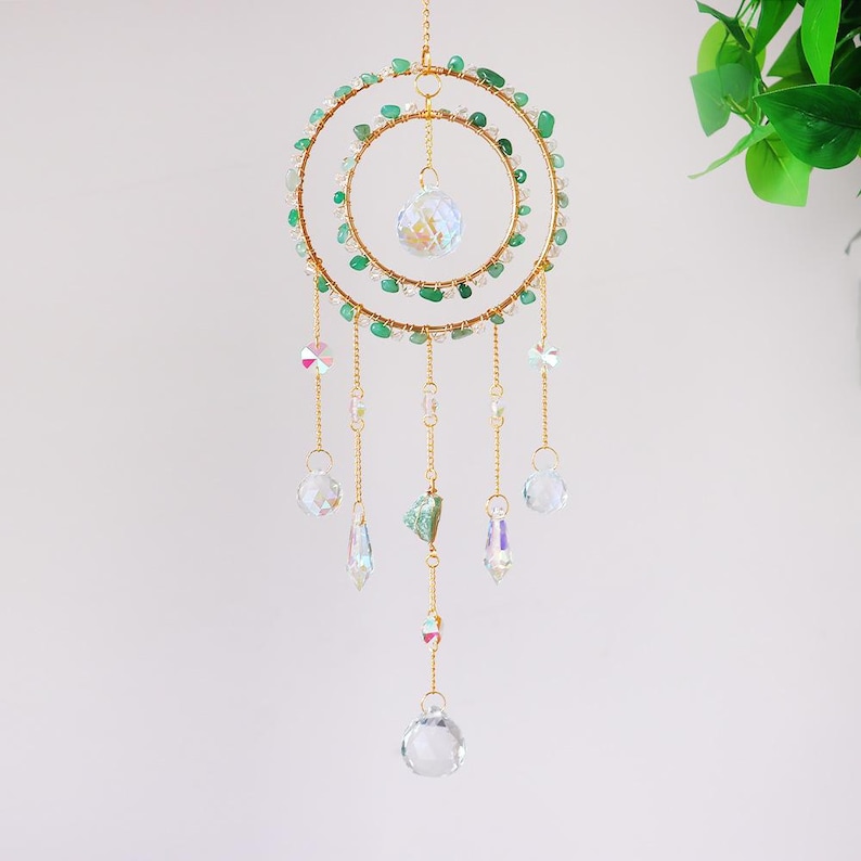 May include: A decorative suncatcher featuring two gold-colored rings adorned with green and clear beads. Clear crystal pendants and a large crystal ball hang from the rings. The suncatcher is designed to hang and catch the light.