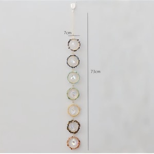 May include: A decorative hanging crystal suncatcher, approximately 28.7 inches (73 cm) long, with seven circular crystal and gemstone accents. Each accent is about 2.75 inches (7 cm) in diameter, featuring a central crystal surrounded by colorful stones.