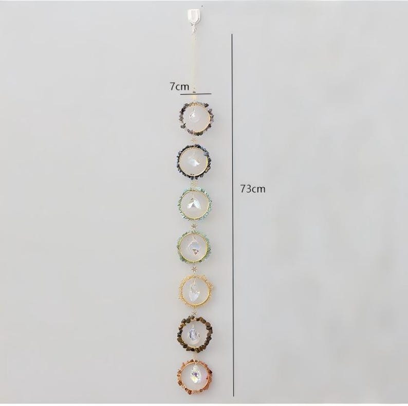 May include: A decorative hanging crystal suncatcher, approximately 28.7 inches (73 cm) long, with seven circular crystal and gemstone accents. Each accent is about 2.75 inches (7 cm) in diameter, featuring a central crystal surrounded by colorful stones.