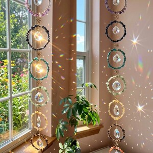 May include: A set of hanging crystal suncatchers with colorful gemstone rings. Each ring features a central crystal pendant and is connected by a delicate gold chain. The gemstones include amethyst, black tourmaline, turquoise, and citrine, creating a rainbow effect.