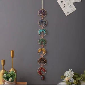 May include: A wall hanging featuring seven circular designs, each with a wire tree filled with colorful gemstones. The gemstones include purple, blue, turquoise, green, yellow, brown, and red. The circles are connected by a gold-colored chain.