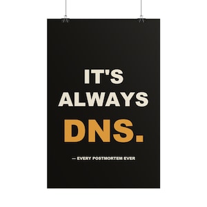 May include: A rectangular black poster hanging from two silver clips. The text reads IT'S ALWAYS DNS. in large white and gold letters, followed by the smaller white text - EVERY POSTMORTEM EVER centered at the bottom of the print.
