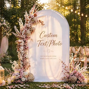 Peut inclure: Décoration de cérémonie de mariage en extérieur avec une arche blanche ornée de compositions florales roses et crème. L'arche porte l'inscription "Custom Text/Photo". Bougies et chaises sont présentes.