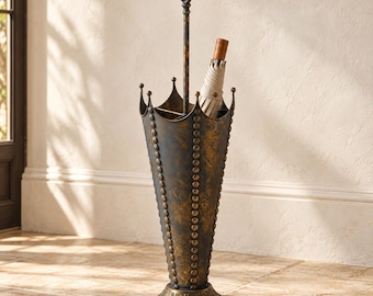 May include: A dark metal umbrella stand shaped like an inverted umbrella with a distressed bronze and black finish. It features a central handle with a decorative top, vertical rows of raised studs, and a scalloped rim. One beige umbrella is inside.