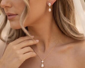 May include: A gold necklace and matching drop earrings set featuring teardrop-shaped white pearls suspended from small, clear, faceted stones. The jewelry set is crafted with thin gold chains and gold metal settings for the stones and pearls.