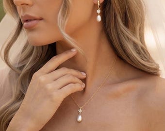 May include: A gold necklace and matching drop earrings set featuring a delicate gold chain and hoop-style earrings. Each piece is adorned with a small, clear, star-shaped crystal accent and a single, smooth, white teardrop-shaped pearl pendant.