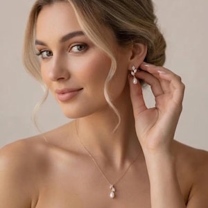 Puede incluir: Una mujer lleva un conjunto de collar y pendientes de oro. La joyer&iacute;a presenta un dise&ntilde;o de hoja con una perla colgante. Los pendientes tienen forma de hoja con una gota de perla. El collar tiene un colgante de hoja a juego con una perla.