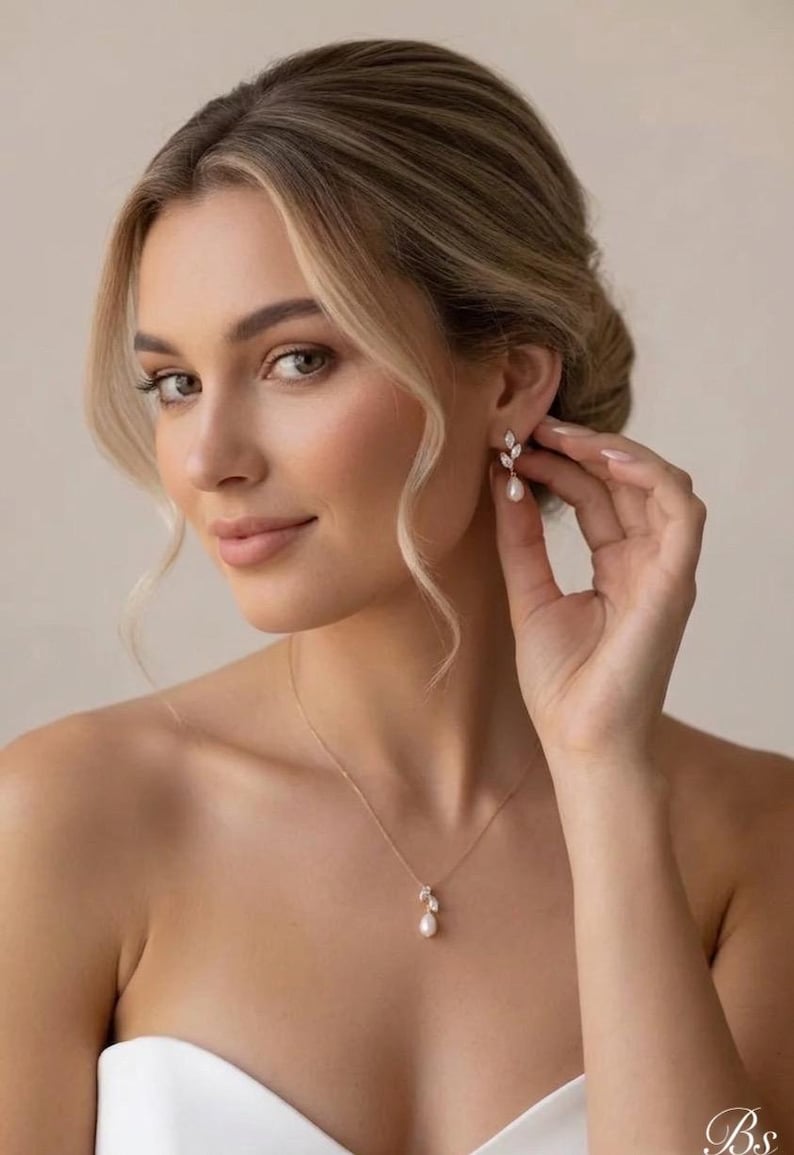 Puede incluir: Una mujer lleva un conjunto de collar y pendientes de oro. La joyer&iacute;a presenta un dise&ntilde;o de hoja con una perla colgante. Los pendientes tienen forma de hoja con una gota de perla. El collar tiene un colgante de hoja a juego con una perla.