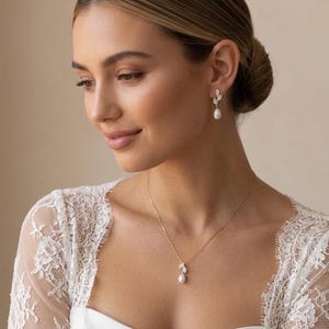 Puede incluir: Una mujer que lleva un collar de oro y pendientes a juego. El collar y los pendientes presentan un dise&ntilde;o de hoja con peque&ntilde;as piedras transparentes y una perla colgante. Lleva una blusa de encaje blanco.