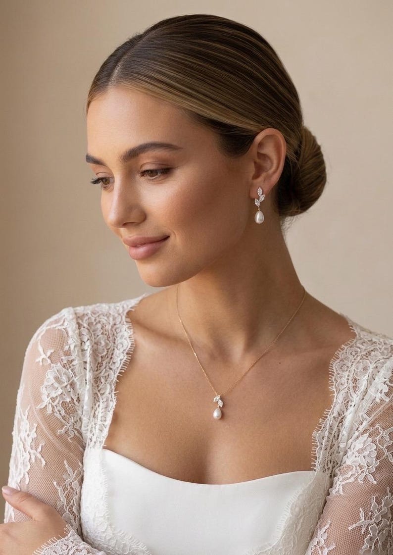 Puede incluir: Una mujer que lleva un collar de oro y pendientes a juego. El collar y los pendientes presentan un dise&ntilde;o de hoja con peque&ntilde;as piedras transparentes y una perla colgante. Lleva una blusa de encaje blanco.
