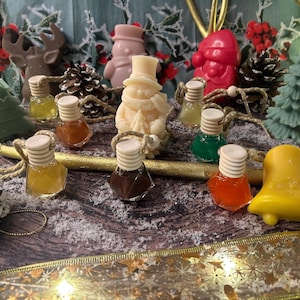 Peut inclure: Une composition festive avec des savons miniatures sur le thème de Noël et des flacons décoratifs. Les savons comprennent un bonhomme de neige, le Père Noël, un renne et un sapin. Les flacons sont remplis de liquides colorés, sur une surface enneigée.