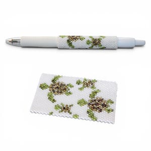 May include: A white pen with a beaded sleeve featuring a turtle design in shades of green and brown. A matching beaded rectangle with the same turtle pattern is also shown.