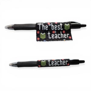 May include: Two black pens with beaded sleeves. The sleeves are black with the words "The best Teacher" in white, along with small colorful flower and book designs. The pens are on a white background.