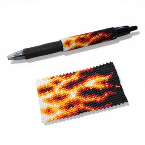 May include: A black pen with a beaded sleeve featuring a flame design in red, orange, yellow, and white. A matching beaded rectangle is also present, showcasing the same flame pattern. The pen has a black rubber grip.