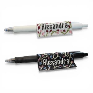 May include: Two pens with beaded name tags. One pen is white with a floral design and the name "Alexandra". The other pen is black with a black, blue, and pink design and the name "Alexandra".