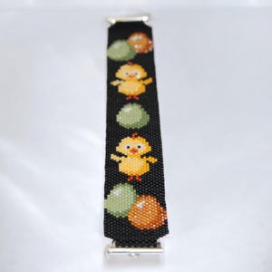 May include: Black beaded bracelet featuring yellow chicks and colorful eggs. The bracelet has a silver clasp and is designed with a repeating pattern of chicks and eggs. The bracelet is approximately 0.75 inches wide.