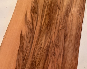 May include: Close-up of a piece of wood with a natural grain pattern. The wood has a reddish-brown hue with darker brown, swirling patterns. The wood grain is visible, creating a textured appearance. The wood appears to be a solid, single piece.