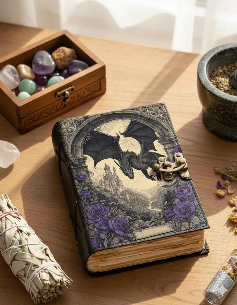 May include: A leather-bound journal with a fantasy dragon and castle design. The cover features a black dragon soaring over a castle, with purple roses. The journal has a metal clasp and aged paper pages.