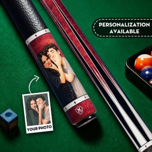 May include: A pool cue featuring a custom printed illustration of a couple on the shaft, with a black textured grip, white and red diamond accents, and a logo. A small photo print shows the original image, and text reads PERSONALIZATION AVAILABLE.