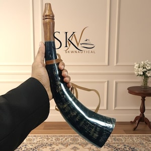 Könnte beinhalten: Ein dunkelblaues Horn mit Holzgriff und Lederriemen. Das Horn hat eine gebogene Form und eine polierte Oberfläche. Der Griff ist hellbraun. Das Horn wird in der Hand einer Person gehalten.