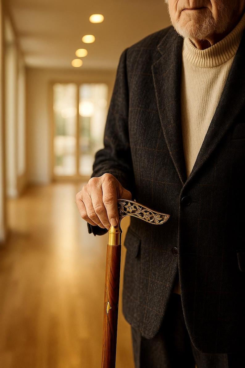 May include: A dark brown wooden cane with a gold-colored handle and decorative floral design. The cane is held by a person wearing a dark gray blazer and a cream-colored turtleneck sweater.