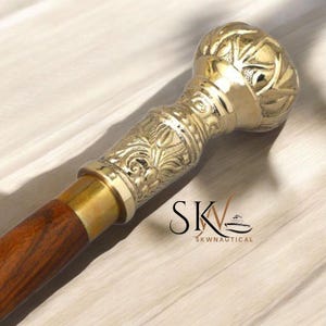 Könnte beinhalten: Dekorativer Gehstock mit poliertem Messinggriff und dunklem Holzschaft. Der Griff weist aufwendige florale und geometrische Muster auf. Der Stock ist für Unterstützung und Stil konzipiert, geeignet für Sammler oder Personen, die Hilfe benötigen.