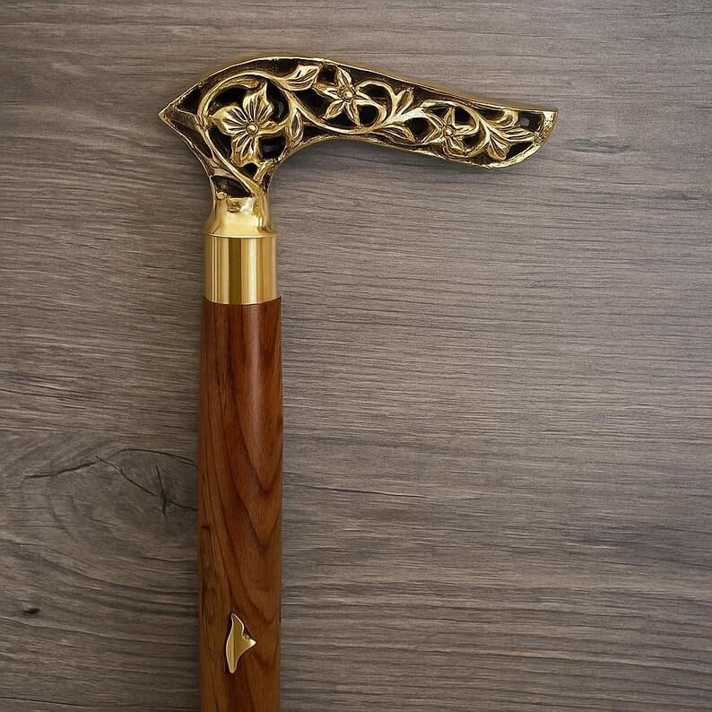 May include: A wooden walking cane with a decorative gold-colored handle. The handle features an intricate floral design. The shaft is a rich brown color, and the handle is accented with gold-colored metal.