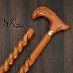 May include: A wooden cane with a curved handle and a twisted shaft. The cane is a warm brown color with a brass collar. The logo "SKWNAUTICAL" is visible in the upper left corner. The cane is designed for support and style.