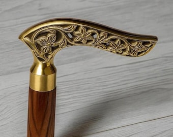 May include: A wooden walking cane with a brass handle. The handle is intricately carved with floral and leaf patterns. The brass collar and the wooden shaft are visible. The cane is a classic accessory.