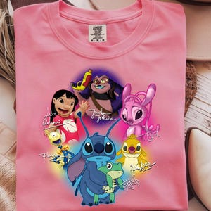 Op de afbeelding: Een roze Comfort Colors t-shirt met een kleurrijke afbeelding van personages uit de animatiefilm Lilo & Stitch. Het ontwerp bevat Stitch, Lilo en andere personages met hun namen in cursief.