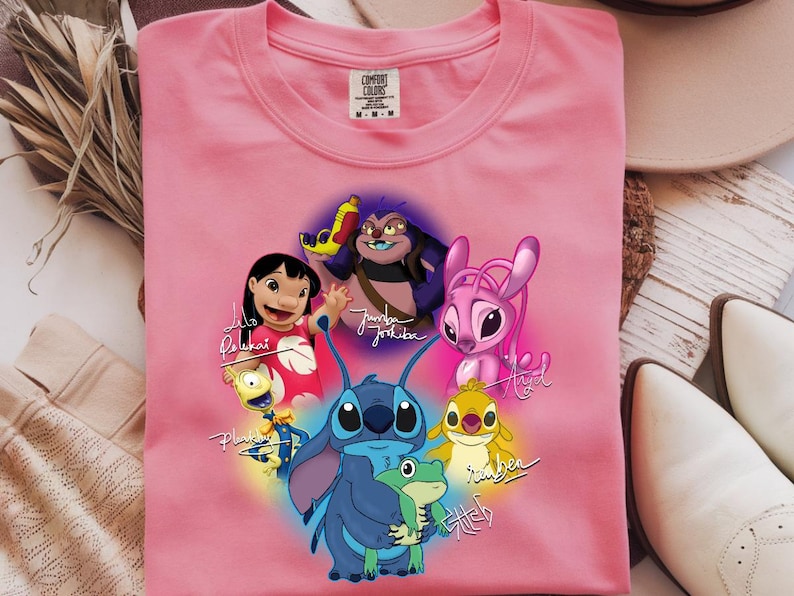 Op de afbeelding: Een roze Comfort Colors t-shirt met een kleurrijke afbeelding van personages uit de animatiefilm Lilo & Stitch. Het ontwerp bevat Stitch, Lilo en andere personages met hun namen in cursief.