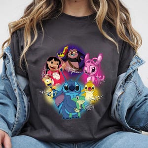 Op de afbeelding: Donkergrijs T-shirt met een kleurrijke afbeelding van personages uit de animatiefilm Lilo & Stitch. Het ontwerp bevat Stitch, Lilo, Angel en andere personages, met hun namen in sierlijke letters. Het T-shirt is gemaakt van een zacht materiaal.