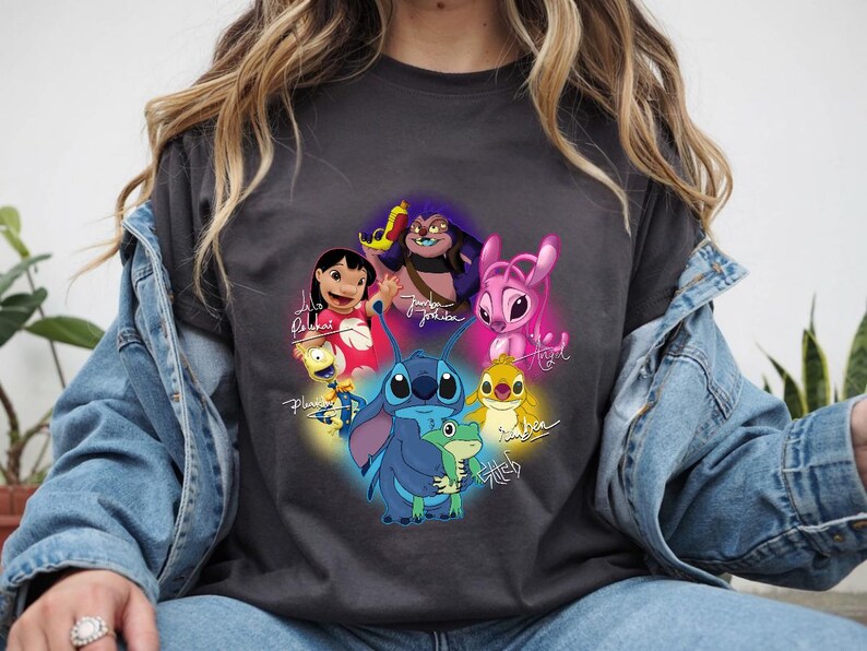 Op de afbeelding: Donkergrijs T-shirt met een kleurrijke afbeelding van personages uit de animatiefilm Lilo & Stitch. Het ontwerp bevat Stitch, Lilo, Angel en andere personages, met hun namen in sierlijke letters. Het T-shirt is gemaakt van een zacht materiaal.