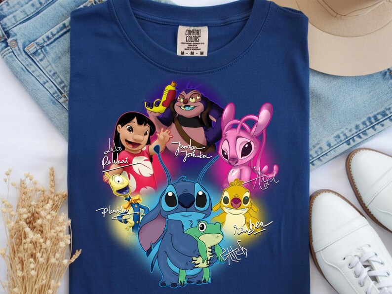 Op de afbeelding: Een marineblauw t-shirt met een kleurrijke afbeelding van personages uit de animatiefilm "Lilo & Stitch". Het ontwerp bevat Stitch, Lilo en andere personages met hun namen in een gestileerd lettertype. Het shirt heeft een ronde hals en korte mouwen.