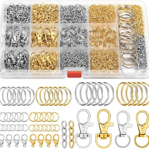 May include: A clear plastic organizer filled with various jewelry-making supplies. The compartments contain silver and gold-colored jump rings, lobster clasps, and chain. Additional jump rings and clasps are arranged below the organizer.