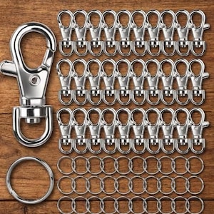May include: A collection of silver-toned metal hardware including one large swivel lobster clasp, thirty smaller swivel lobster clasps arranged in three rows, and thirty circular split key rings arranged in three rows below the clasps.