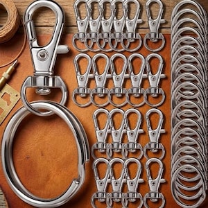 May include: A collection of silver-toned metal hardware including multiple swivel lobster claw clasps and circular split rings. The set features one large lobster clasp attached to a large ring, alongside several smaller clasps and rings arranged in rows.