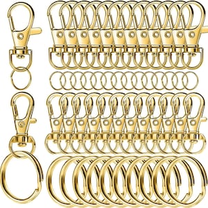 May include: A collection of gold-colored swivel snap hooks, split key rings, and key rings. The snap hooks have a lobster claw design. The key rings are round and come in various sizes. The items are arranged in neat rows, suggesting a bulk supply.