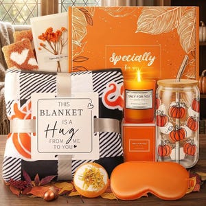 May include: A gift set featuring a black and white plaid blanket with a tag reading THIS BLANKET IS A HUG FROM ME TO YOU, an orange box labeled Specially for you, a candle, a glass tumbler with pumpkin prints, a bath bomb, and an orange sleep mask.