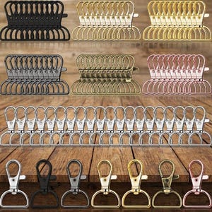 May include: A collection of metal swivel lobster claw clasps with D-ring attachments, arranged in multiple rows. The set includes various metallic finishes such as matte black, bright gold, antique brass, rose gold, and polished silver tones.