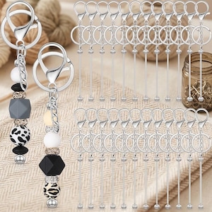 May include: A collection of silver-toned metal keychain hardware featuring a split ring and a lobster clasp attached to a long, thin rod with a small ball end. Two fully assembled keychains include decorative silicone and rhinestone beads.