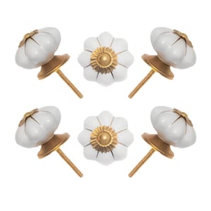 May include: Six white ceramic cabinet knobs with a flower design and gold-colored accents. The knobs have a gold-colored base and screw. The knobs are arranged on a white background.