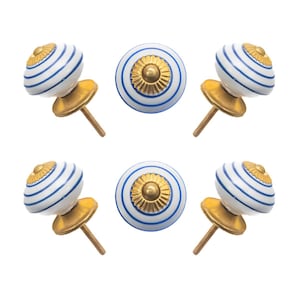 May include: Six decorative cabinet knobs. The knobs are white with blue stripes and a gold-colored center. The base and screw are gold-colored. The knobs are arranged in a circular pattern against a white background.